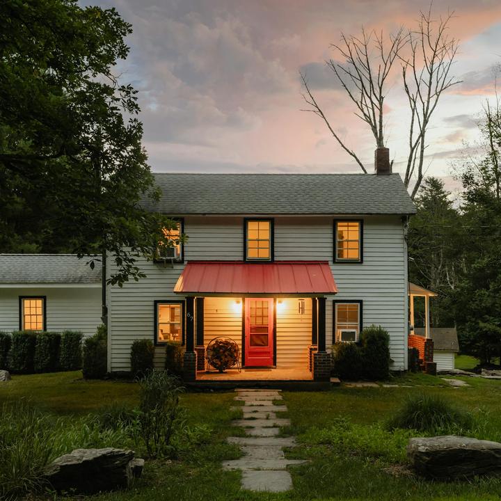 White farmhouse at dusk with warm porch lights and a red front door